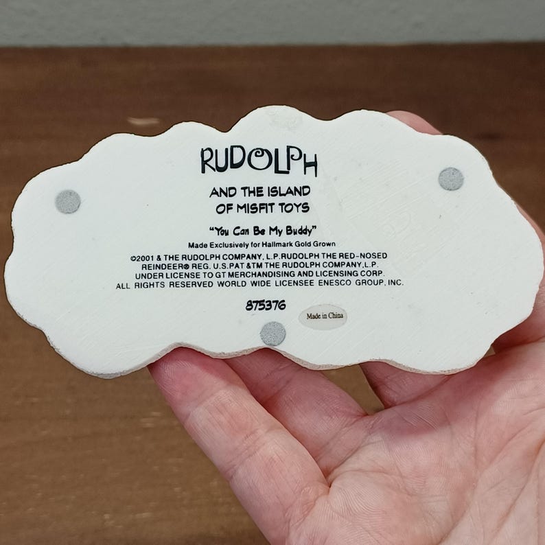 May include: A white ceramic figurine with the text "RUDOLPH AND THE ISLAND OF MISFIT TOYS" and "You Can Be My Buddy". The figurine is in the shape of a cloud and includes the number 875376.