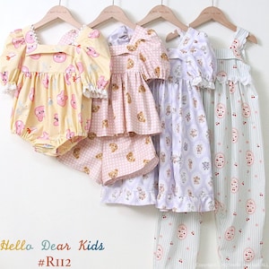 May include: Four children's outfits hanging on wooden hangers. The outfits include a yellow romper, a pink gingham top and shorts set, a lavender dress, and a striped pajama set. Each garment features a repeating pattern of cartoon characters.
