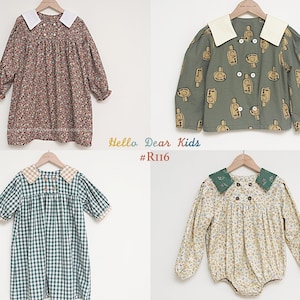 May include: Four children's garments are displayed on wooden hangers. The items include a floral print dress, a green jacket with a bottle pattern, a green and white checkered dress, and a floral romper. The text "Hello Dear Kids #R116" is visible.