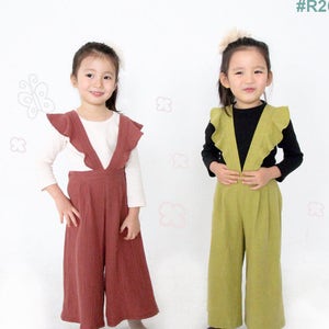 May include: Two young girls wearing matching ruffled-top jumpsuits. One jumpsuit is a reddish-brown color, paired with a white long-sleeve shirt. The other is a light green jumpsuit with a black long-sleeve shirt. The text "Hello Dear Kids #R26" is visible.