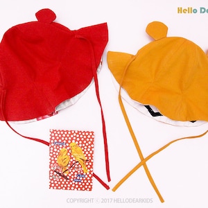 May include: Two sun hats with ear flaps in red and yellow. The hats have ties that can be tied under the chin. The hats are on a white background. #A2