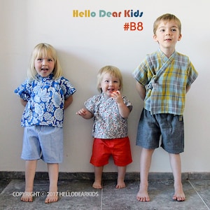 以下が含まれることがあります： 異なる柄のシャツとショートパンツを着た3人の子供。右側の男の子は、チェック柄のシャツとグレーのショートパンツを着用しています。真ん中の女の子は、花柄のシャツと赤いショートパンツを着用しています。左側の女の子は、青と白の花柄のシャツと青と白のギンガムチェックのショートパンツを着用しています。子供たちの頭上に「Hello Dear Kids #B8」という文字が書かれています。