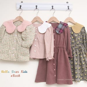 Puede incluir: Cuatro conjuntos infantiles colgados en una pared blanca. Los conjuntos incluyen una chaqueta con estampado floral y cuello rosa, una blusa rosa con lunares, un vestido de pana malva y un vestido con estampado floral y cuello amarillo. El texto "Hello Dear Kids #Ri08" es visible.