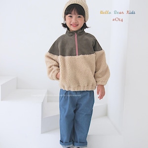 Pu&ograve; includere: Un bambino indossa una giacca di pile marrone e beige con una cerniera rosa, jeans blu e un berretto di lana bianco con un pon pon. Il testo "Hello Dear Kids #014" &egrave; nell'angolo in alto a destra dell'immagine.
