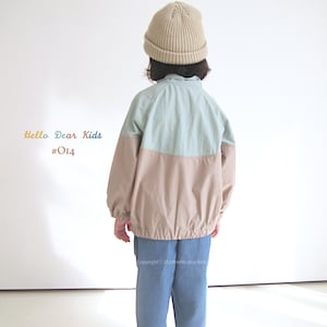 Pu&ograve; includere: Un bambino indossa una giacca blu chiaro e beige con un berretto beige. La giacca ha una cerniera e un cordoncino in vita. Il bambino indossa anche jeans blu e scarpe da ginnastica bianche. Il testo "Hello Dear Kids #014" &egrave; visibile nell'immagine.