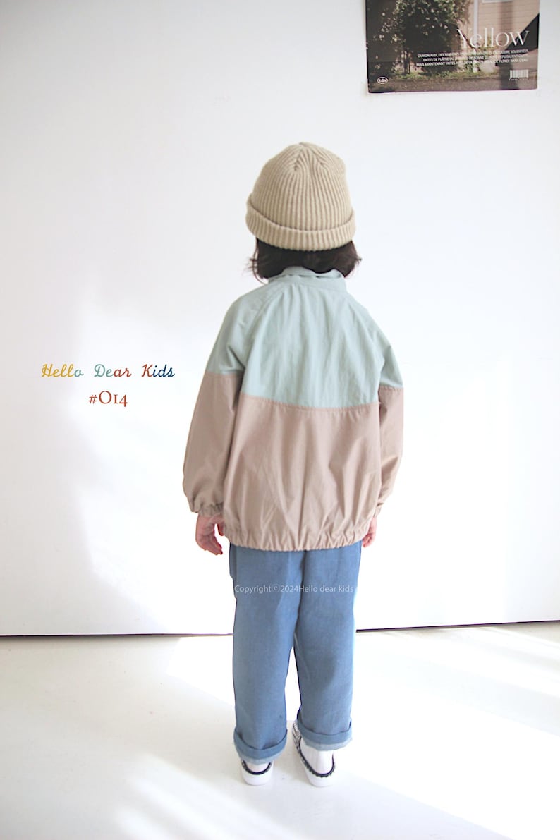 Pu&ograve; includere: Un bambino indossa una giacca blu chiaro e beige con un berretto beige. La giacca ha una cerniera e un cordoncino in vita. Il bambino indossa anche jeans blu e scarpe da ginnastica bianche. Il testo "Hello Dear Kids #014" &egrave; visibile nell'immagine.
