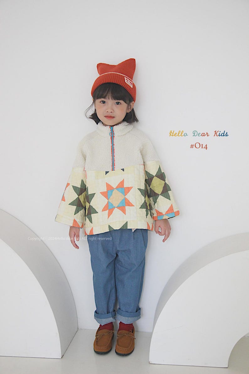Pu&ograve; includere: Un bambino indossa una giacca trapuntata bianca e gialla con un motivo a stelle, jeans blu, scarpe marroni e un cappello di lana arancione con un logo. Il testo "Hello Dear Kids #014" &egrave; visibile nell'immagine.