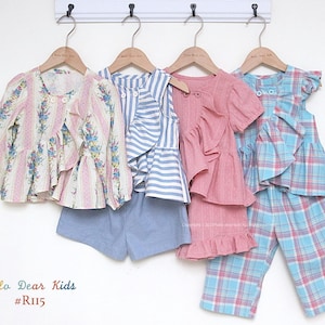 May include: Four children's outfits hanging on wooden hangers. The outfits include a floral print top, striped top with blue shorts, a pink ruffled top, and a blue plaid top and pants set. The text "Hello Dear Kids #R115" is at the bottom.