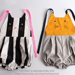 May include: Two baby onesies with cat faces. One onesie is black and white striped with pink straps. The other onesie is gray with a yellow cat face and black straps. The text "H.D.K R1" is in the top left corner of the image.