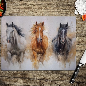 May include: Three horses running in a watercolor style. The horses are a white horse, a brown horse, and a black horse. The background is a light gray with splashes of color.