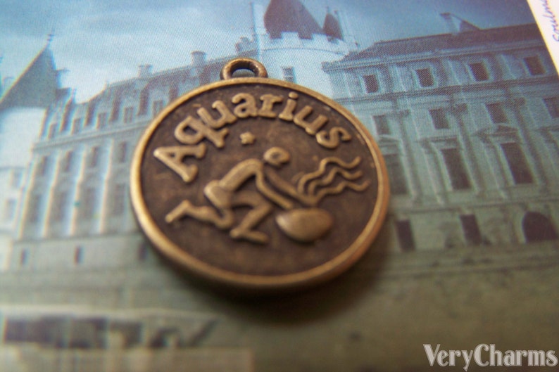 May include: A bronze-colored metal charm with the word "Aquarius" and a stylized image of the astrological sign.