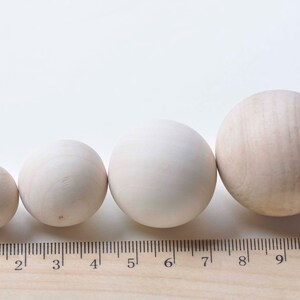 Puede incluir: Cuatro bolas de madera de diferentes tama&ntilde;os, que van desde 2,5 a 10 cm de di&aacute;metro, est&aacute;n alineadas en una regla de madera. Las bolas son de color beige claro y tienen un acabado liso y pulido.