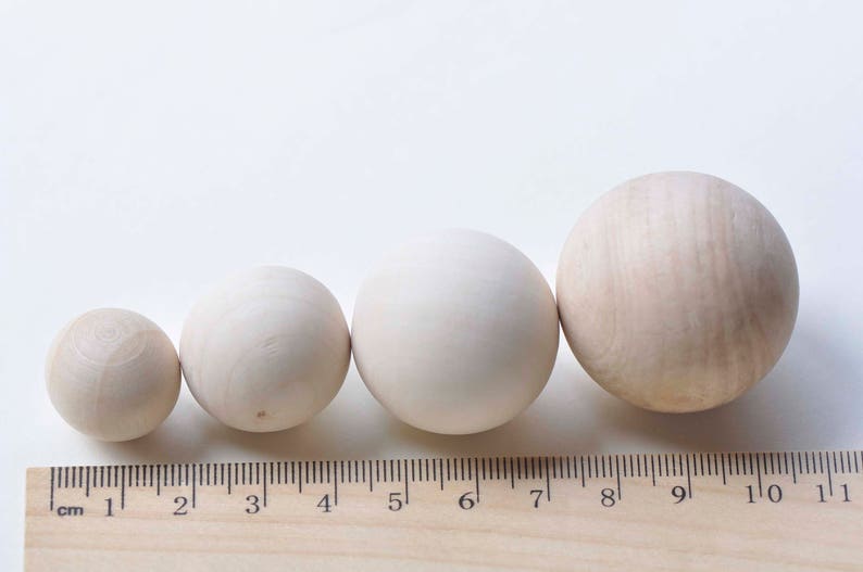Puede incluir: Cuatro bolas de madera de diferentes tama&ntilde;os, que van desde 2,5 a 10 cm de di&aacute;metro, est&aacute;n alineadas en una regla de madera. Las bolas son de color beige claro y tienen un acabado liso y pulido.