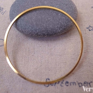 Può includere: Un braccialetto rigido dorato, su una superficie di tessuto beige. Il braccialetto è rotondo e ha una finitura liscia e lucida.