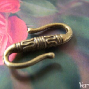 May include: A gold-toned metal hook with an ornate design. The hook is shaped like a letter 'S' and has a smooth, polished finish.