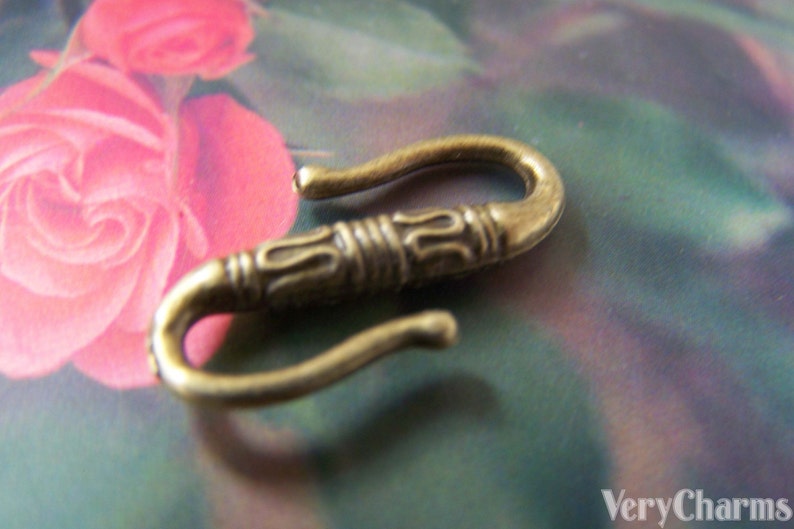 May include: A gold-toned metal hook with an ornate design. The hook is shaped like a letter 'S' and has a smooth, polished finish.