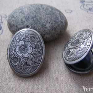 May include: Two silver oval locket pendants with a floral design. The lockets are open and closed.