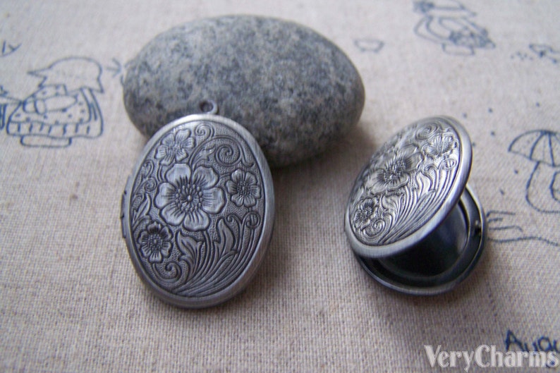 May include: Two silver oval locket pendants with a floral design. The lockets are open and closed.