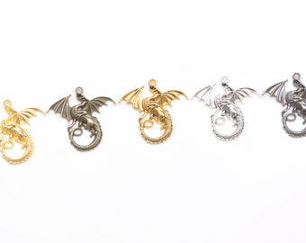 May include: Five dragon charms in different finishes: gold, bronze, silver, antique silver, and black. Each charm features a detailed dragon design with wings outstretched and a curled tail.