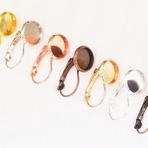 Può includere: Sette paia di basi per orecchini con diverse finiture metalliche: oro, argento, oro rosa, bronzo e bronzo scuro. Ogni base ha un cabochon rotondo in vetro trasparente.