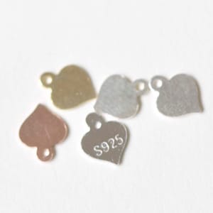 Puede incluir: Cuatro dijes de metal en forma de corazón en diferentes colores: dorado, plateado, dorado rosa y plateado con la inscripción "S925".