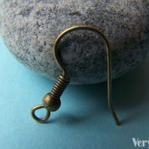 May include: A bronze-colored earring hook with a coiled wire and a small ball at the top. The hook is designed for attaching jewelry findings.