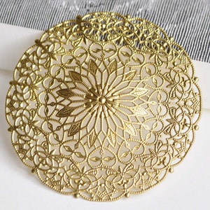 May include: A gold-coloured metal filigree circle with a detailed floral design. The circle is approximately 7.5 cm in diameter.