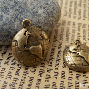 May include: Two antique gold-toned metal globe charms with a raised map design. The charms have a loop at the top for attaching to jewelry or other crafts.