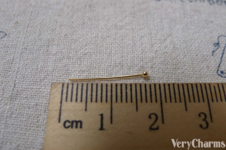 May include: A gold-colored head pin measuring 1 inch in length. The pin has a small round head and is shown next to a ruler.