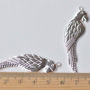 May include: Two silver metal parrot charms with a detailed design. The charms are approximately 5 cm and 7 cm long.