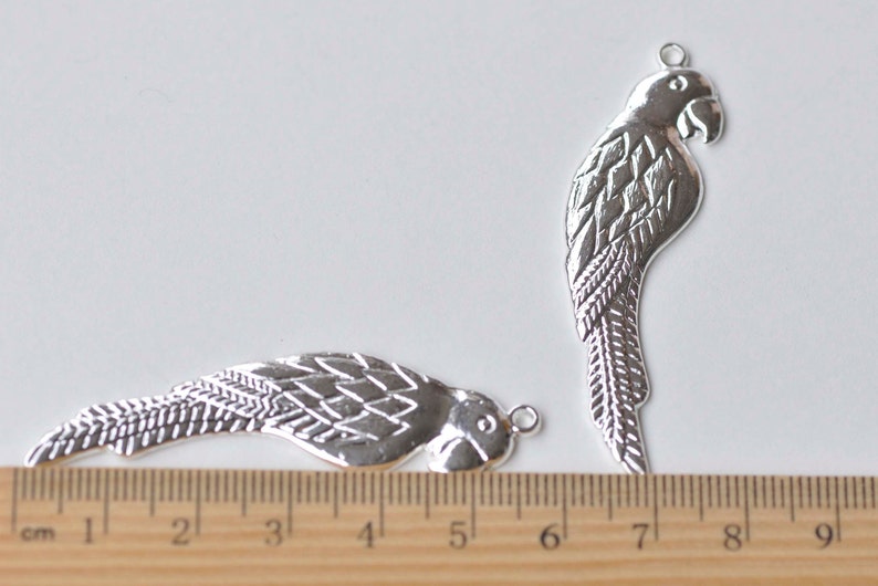 May include: Two silver metal parrot charms with a detailed design. The charms are approximately 5 cm and 7 cm long.