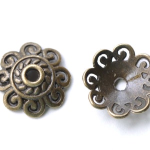 Könnte beinhalten: Zwei antike, goldfarbene Metallperlenkappen mit einem dekorativen Blumenmuster. Die Kappen haben ein rundes Loch in der Mitte.