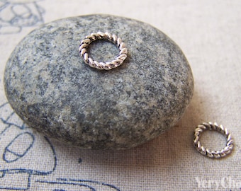 May include: Two silver-toned twisted wire rings. The rings are on a gray stone and a beige fabric background.