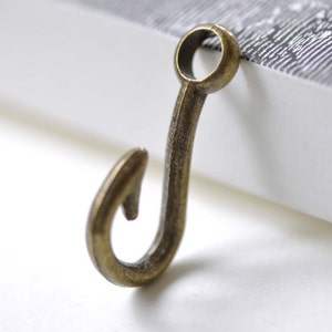 Pode incluir: Um pequeno gancho de metal dourado antigo com um laço no topo. O gancho tem aproximadamente 2,5 cm de comprimento.