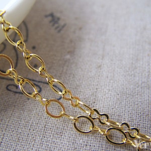 May include: Gold chain with oval links. The chain is on a light brown fabric background.