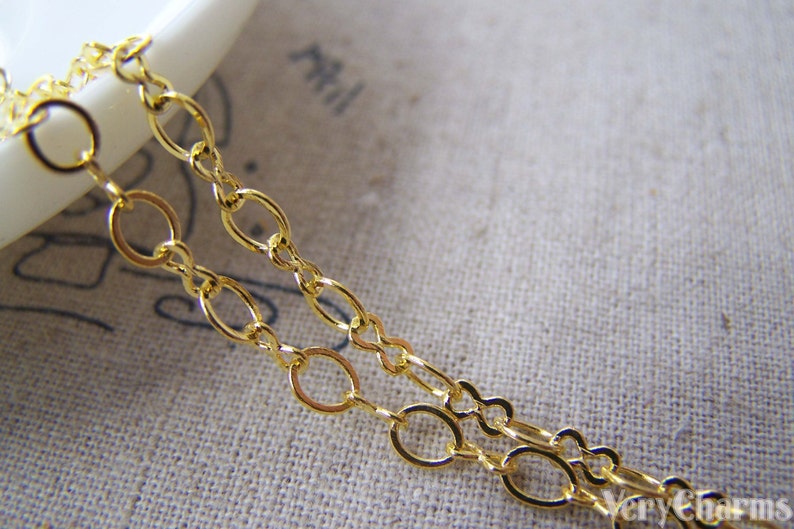 May include: Gold chain with oval links. The chain is on a light brown fabric background.