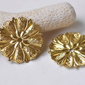 May include: Two gold-toned metal decorative embellishments with a floral design. Each embellishment has a central hole.