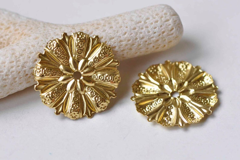 May include: Two gold-toned metal decorative embellishments with a floral design. Each embellishment has a central hole.