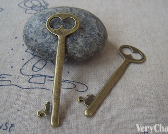 May include: Two antique-style brass keys with intricate details. The keys have a heart-shaped hole in the bow and a decorative design on the bottom. The keys are on a beige fabric background.