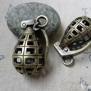 Puede incluir: Dos abalorios de granada de metal dorado antiguo con un diseño en forma de jaula. Los abalorios tienen un bucle en la parte superior para sujetarlos a un collar o pulsera.