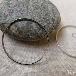 Può includere: Due cerchi in metallo argentato, uno sopra una roccia grigia e l'altro su una superficie di tessuto bianco.