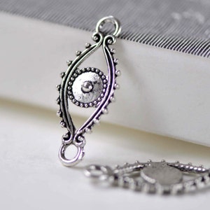 Puede incluir: Encanto de plata con un diseño de ojo, que presenta detalles intrincados y un borde de cuentas. El encanto tiene dos bucles para sujetarlo a joyas.