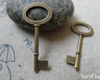 May include: Two antique-style skeleton keys with a brass finish. The keys have a simple design with a round keyhole and a straight shaft. The keys are lying on a textured fabric surface.