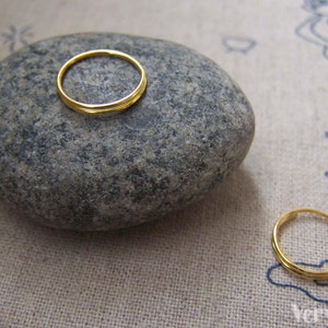 Op de afbeelding: Twee gouden ringen op een grijze steen. De ringen zijn eenvoudig en delicaat, met een gladde afwerking.