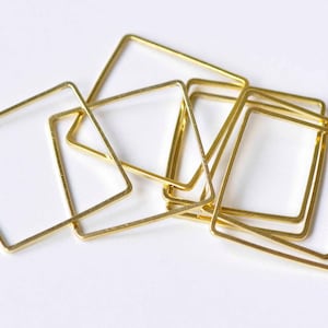 May include: A group of gold-colored metal square hoops of varying sizes. The hoops are stacked and overlapping.
