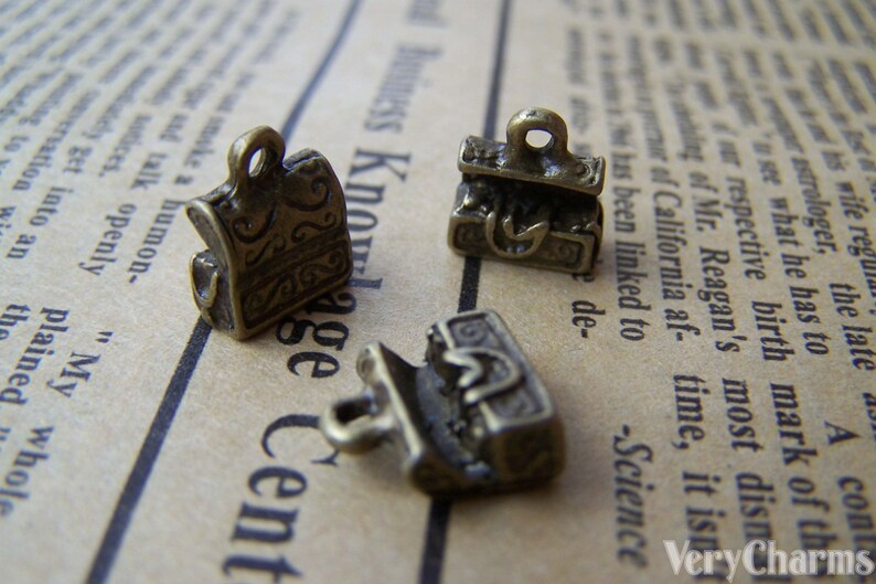 May include: Three antique gold-toned metal charms shaped like treasure chests. The charms have intricate details and are perfect for adding a vintage touch to jewelry or crafts.