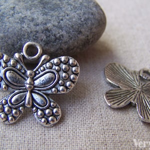 May include: Two silver butterfly charms. One charm has a beaded design and the other has a more detailed, textured design.