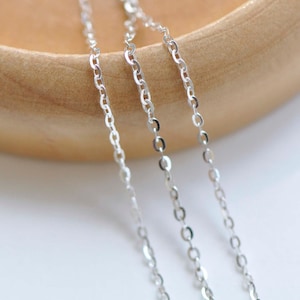 Puede incluir: Tres cadenas de plata de diferentes longitudes y grosores, sobre una superficie de madera.