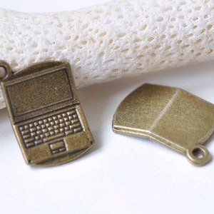 May include: Two antique gold-toned metal charms. One charm is shaped like a laptop computer with a keyboard and a touchpad. The other charm is a simple rectangle with rounded corners.