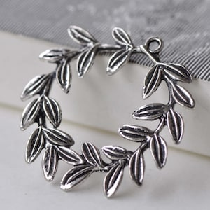 May include: Silver-toned metal wreath charm with a detailed leaf design. The wreath is open at the top and has a loop for hanging.